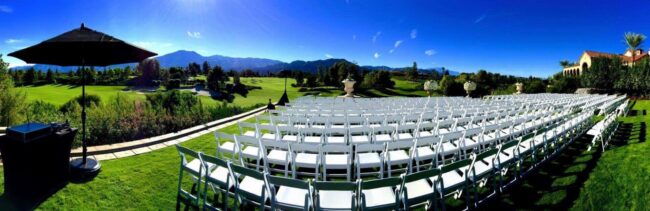 A large outdoor wedding with white folding chairs.