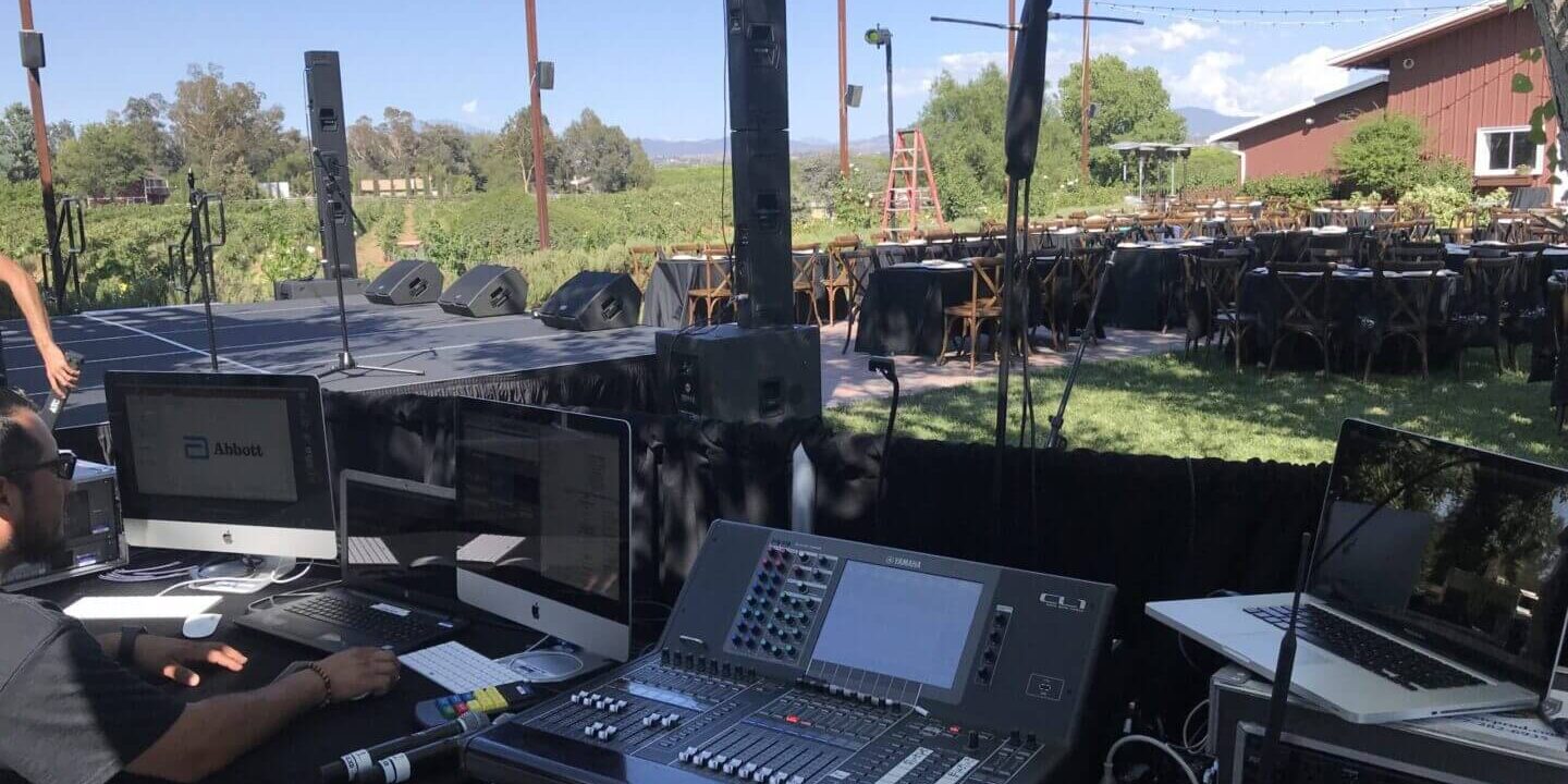 Outdoor stage setup with audio equipment and computers.