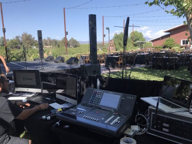 Outdoor stage setup with audio equipment and computers.